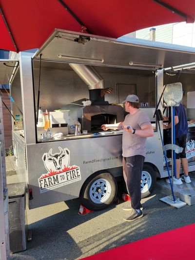 Pizziollo adding pizzas to a wood fired oven on a trailer, Parksville Market