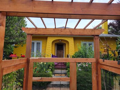Photo of a bright yellow bungalow, framed by a red cedar fence, Oak Bay