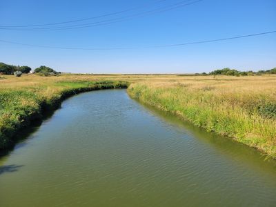 a magical prairie view. calm water of Wascana Creek with tall grass on each bank and a clear blue sky in the distance. Everything is pancake flat.