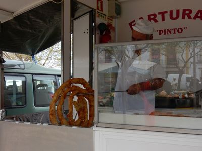 the Fartura vendor removing a large coil of deep fried dough from the oil, using a long metal rod.